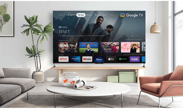 TCL 98 C735 4K QLED TV hængende på bagvæggen af en stue med Google TV på skærmen