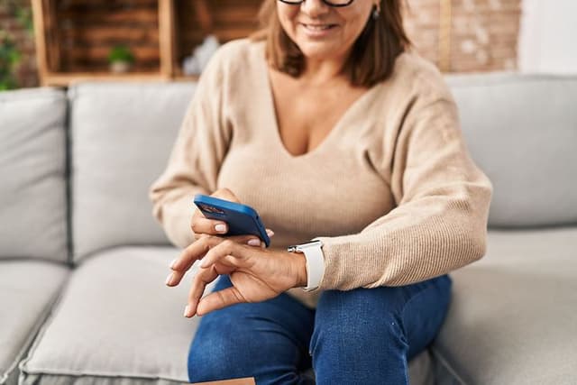 Kvinde der sidder med en smartphone og et smartwatch på håndleddet
