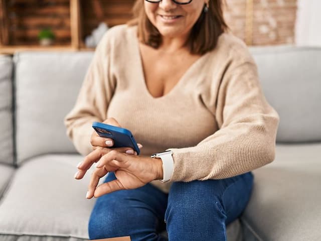 Kvinde der sidder med en smartphone og et smartwatch på håndleddet