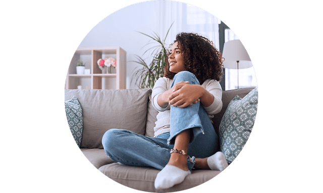 Kvinde der sidder i en sofa med sit ben i sine arme