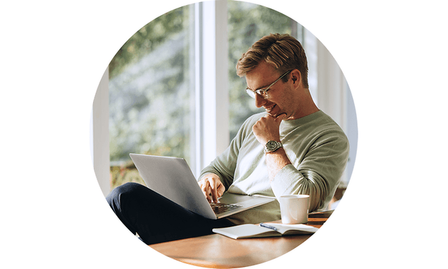 En mand der sidder og arbejder på sin laptop med en kop kaffe på bordet ved siden af ham