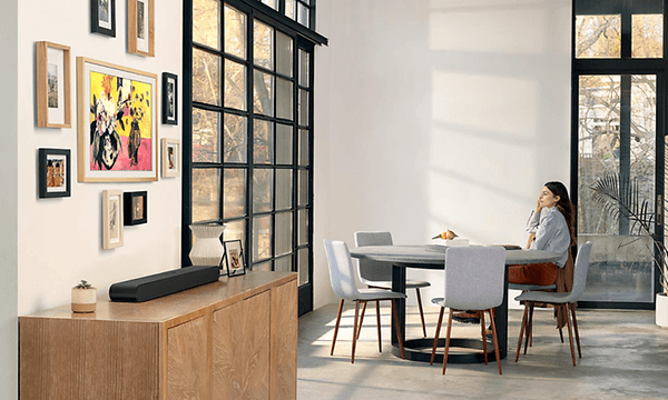 Samsung All-In-One Soundbar på kommode i en stue med kvinne i bakgrunnen