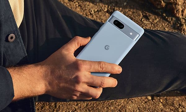 Mann som holder en Google Pixel 7a på en strand
