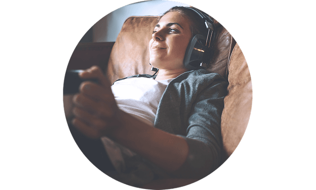Ung kvinde der sidder i en sofa og hører musik med høretelefoner på