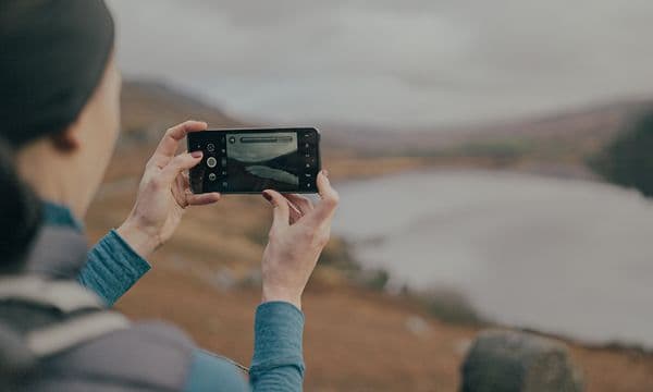 Cat S75 5G smartphone i händerna på en kvinna som tar ett foto av bergslandskapet