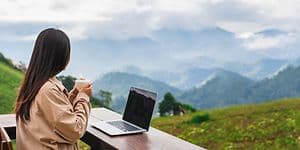 Woman with a laptop and computer staring on a view of nature and mountains