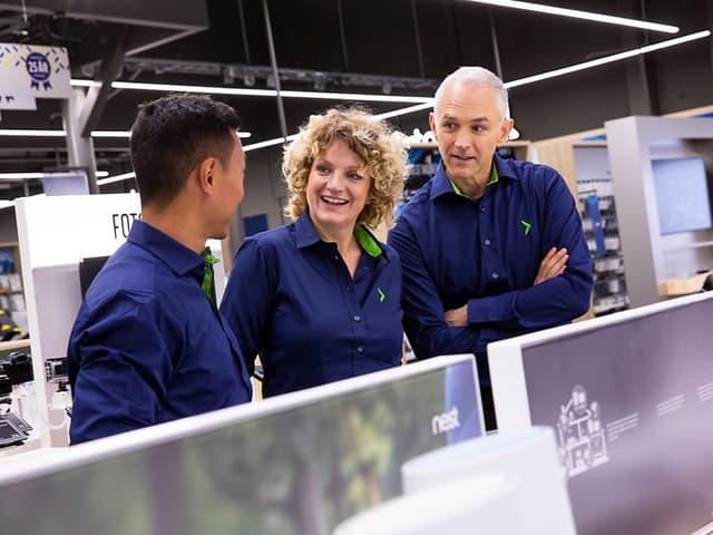 Tre uniformerede Elkjøp-medarbejdere i en Elkjøp-butik