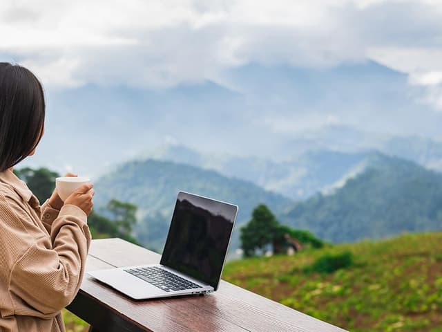 b2b workation - kvinne som ser utover fjellandskap med en kopp kaffe og en laptop