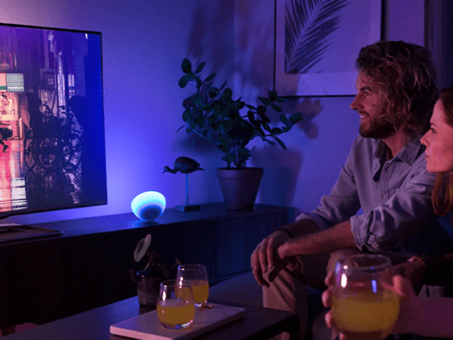 Fyra personer ser på TV med Philips Hue stämningslampor bredvid i lila och blått.