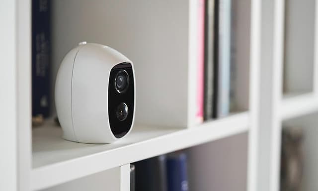A small indoor surveillance camera on a shelf monitoring the living room space