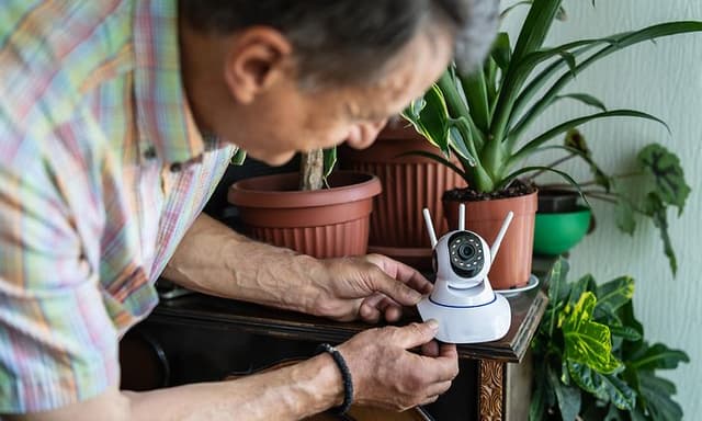 An elderly gentleman setting up an indoor security camera at home