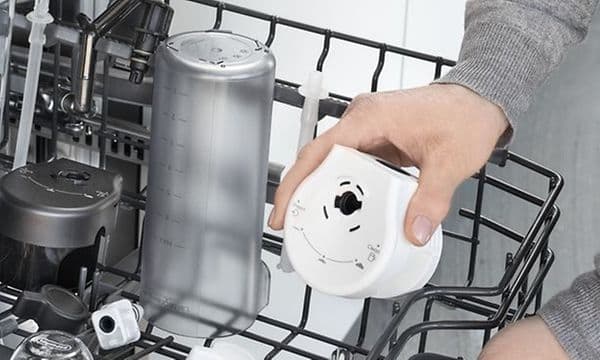 Person som setter Delonghi Eletta Explore-kaffemaskindeler i en oppvaskmaskin