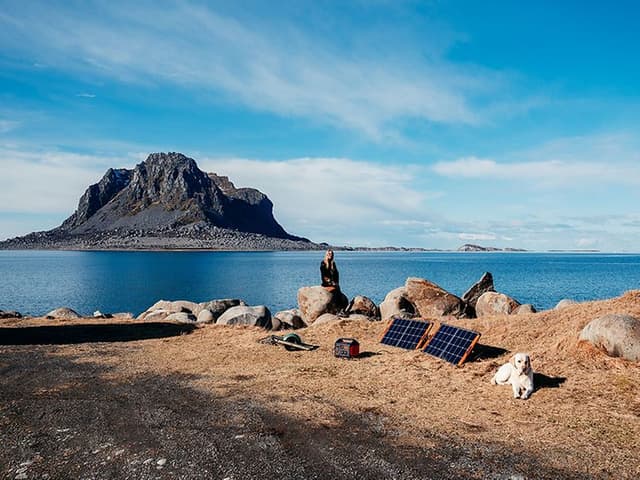 Kvinne som bruker Jackery Explorer bærbare strømkilde og SolarSaga solcellepaneler utendørs ved vannet