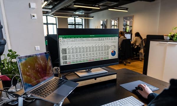 Henkilö työskentelee tietokoneellaan taulukko-ohjelman parissa avokonttorissa