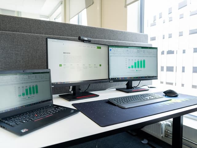 Et kontorskrivebord med laptop, skærme, mus og tastatur.