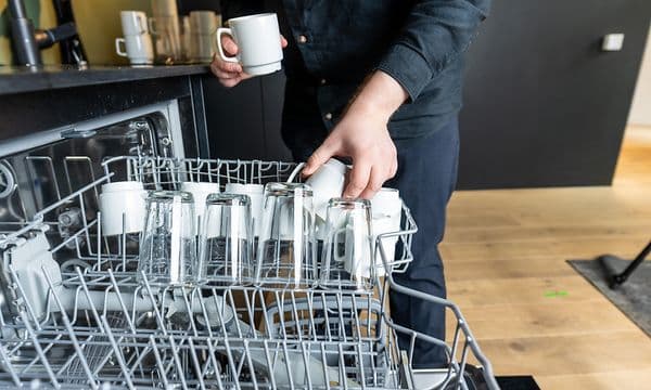 Mann som tømmer en oppvaskmaskin på jobb