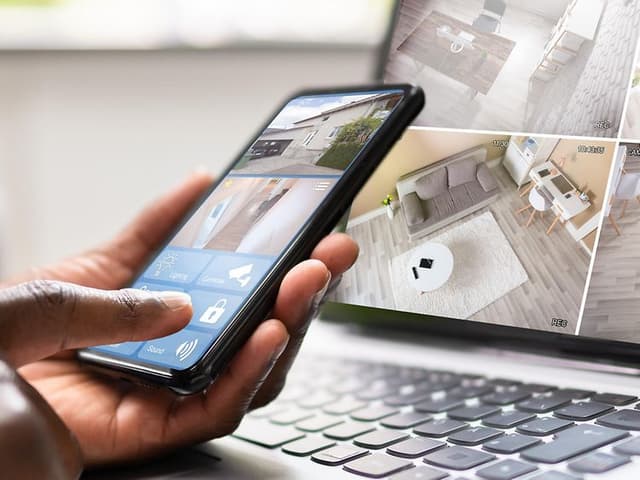 En person det sidder ved en laptop og bruger en telefon og en laptop til at bruge sin overvågning