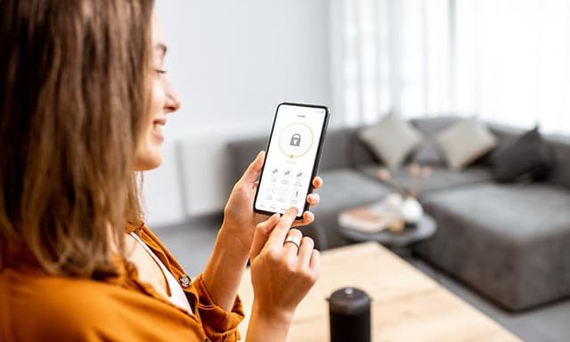 En kvinde der sidder i en stue og bruger en app til at styre hendes overvågning