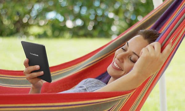 A woman looking at her Pocketbook while chilling on a hammock in the nature surroundings