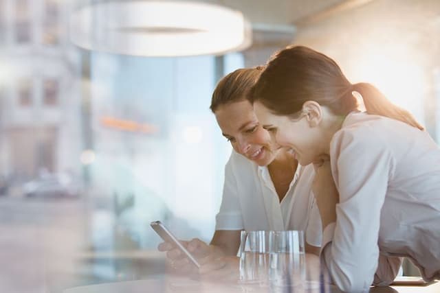 B2B - Telecom - Two women leaning on the table and looking at a phone