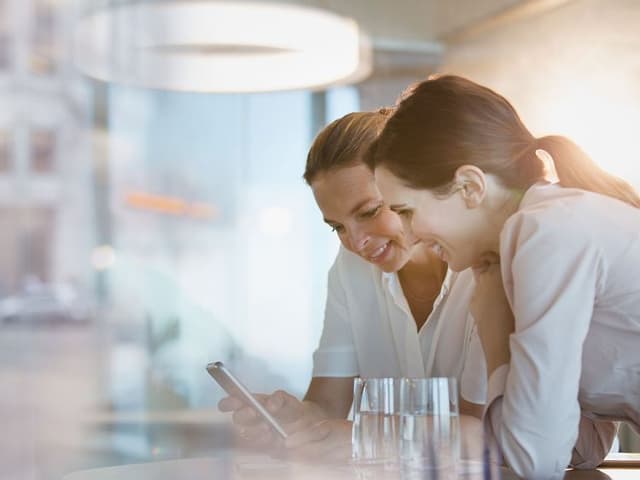 B2B - Telecom - Two women leaning on the table and looking at a phone