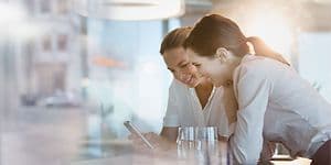 B2B - Telecom - Two women leaning on the table and looking at a phone