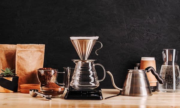 Two types of coffee pots on a wooden table next to coffee beans and ground coffee