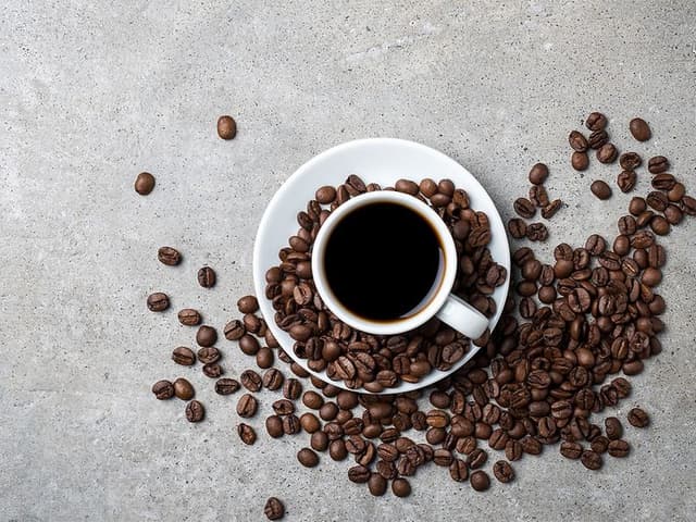Coffee cup with beans scattered around it on a grey table top