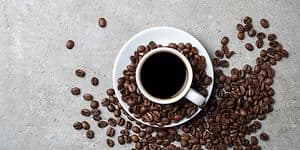 Coffee cup with beans scattered around it on a grey table top