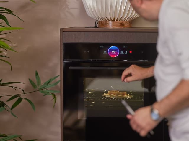 Kokk som damper fisk i plastboks i en Bosch accent line-ovn med dampfunksjon