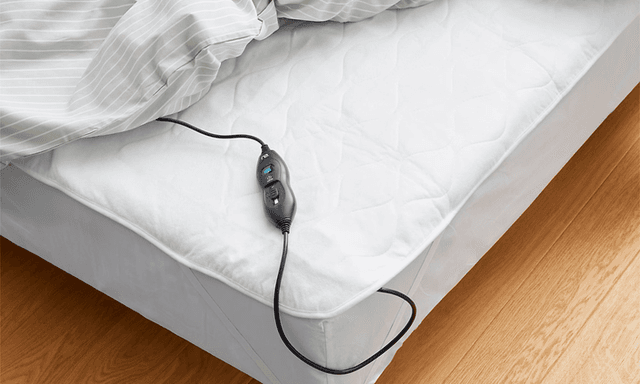 Opvarmning: Elektrisk varmetæppe fra ReLuxury som lagen på en seng med fjernbetjening vist i hjørnet af sengen