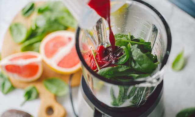 Blender with greens inside and red juice being poured over