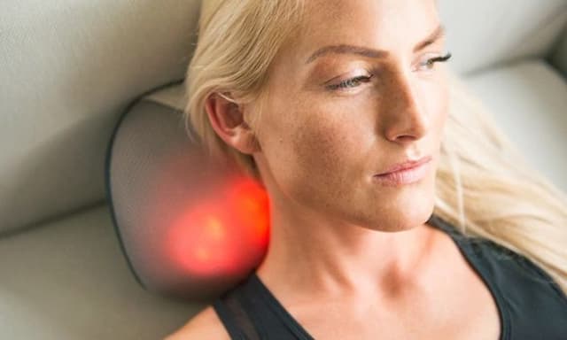 Woman lying on couch massaging her neck with YouCare mini massage pillow