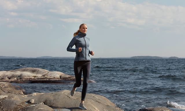 Kvinne jogger nær havet med treningsklær