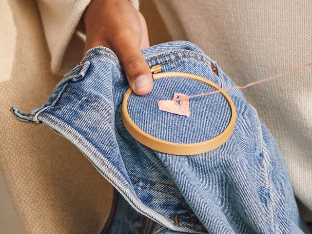 Kvinne som reparerer et par jeans ved å sy et hjerte
