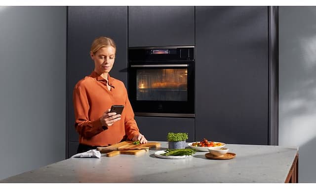 Electrolux innebygd dampovn og kvinne som sjekker oppskriften på telefonen mens hun lager middag
