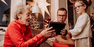 Billede af bedstemor der modtager en gave for barnebarn omgivet af familie i en julestue