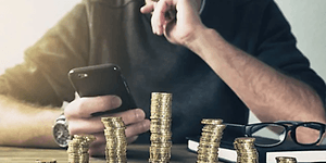 Mann ser på mobil med tårn av kroner foran seg