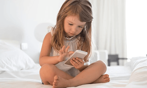 Ung jente sitter i sengen og ser på mobilen