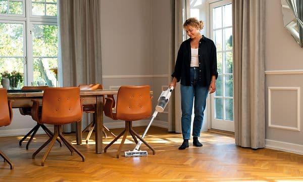 Nainen imuroi parkettilattiaa tuolin alta Nilfisk S1 Home plus -varsi-imurilla