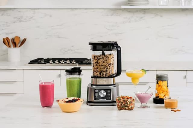 Blender på et køkkenbord med beholdere og glas rundt omkring