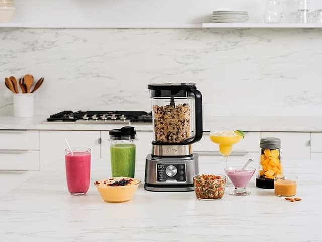 Blender på et køkkenbord med beholdere og glas rundt omkring