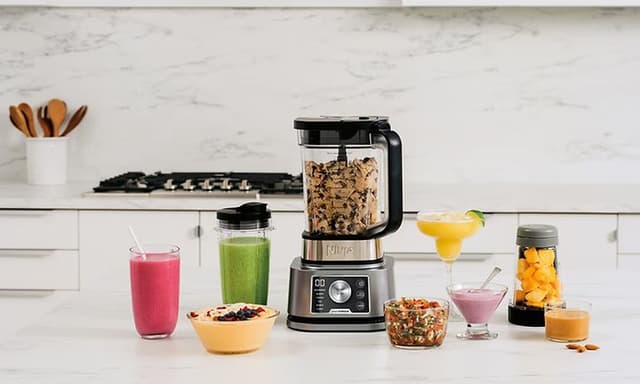 Blender på et køkkenbord med beholdere og glas rundt omkring
