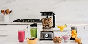 Blender på et køkkenbord med beholdere og glas rundt omkring