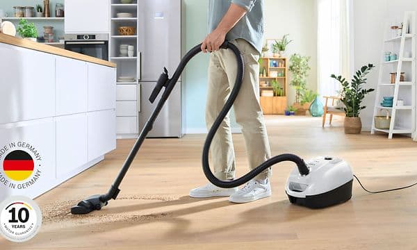 Mies imuroi keittiön lattiaa Bosch Series 4 -pölynimurilla, kuvan vasemmassa alareunassa logo 10 vuoden moottoritakuulle