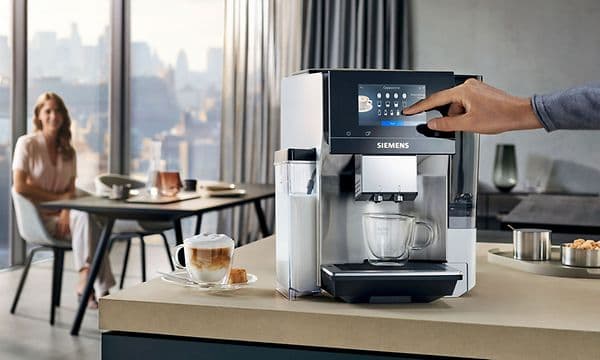 Siemens EQ700 kaffemaskin på köksbänk och en kvinna som sitter vid köksbordet i bakgrunden