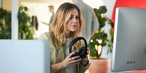 Kvinde foran en PC med Microsoft 365 Office og med hovedtelefoner i hånden