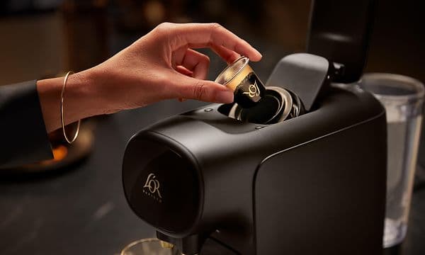 En svart L'OR Barista-kaffemaskin og en person som setter inn en kaffekapsel i den
