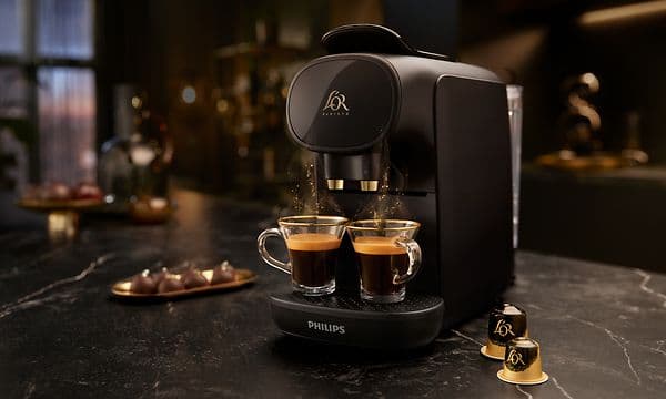 En svart L'OR Barista kapselmaskin og to kopper nybrygget espresso og to espresso kaffekapsler