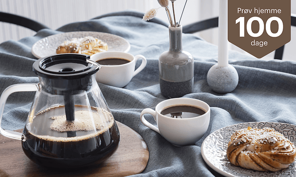 Blooming kaffemaskine på et bord ved siden af kaffekopper og kager